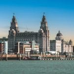 Skyline of Liverpool featuring the Liver Building with its iconic clock towers. The scene is set under a vibrant blue sky, conveying a historic charm.