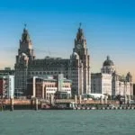 Skyline of Liverpool featuring the Liver Building with its iconic clock towers. The scene is set under a vibrant blue sky, conveying a historic charm.
