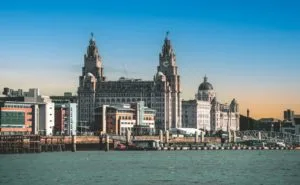 Skyline of Liverpool featuring the Liver Building with its iconic clock towers. The scene is set under a vibrant blue sky, conveying a historic charm.